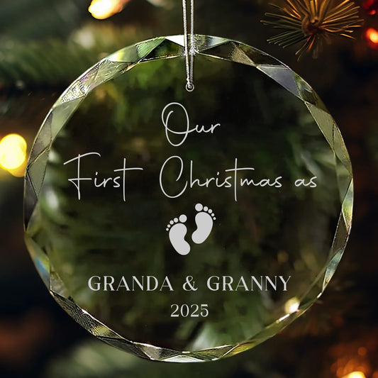 Personalized glass ornament engraved with “Our First Christmas as Granda & Granny 2025” and baby footprints design, hanging on a Christmas tree.