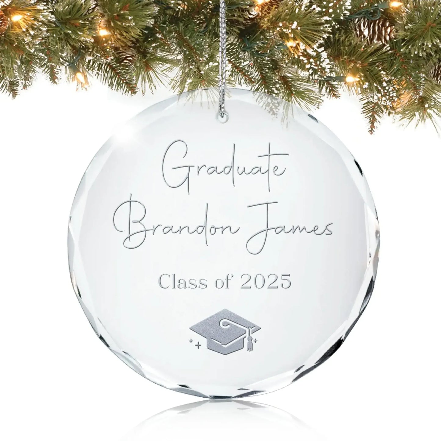 Personalized glass graduation ornament engraved with “Graduate,” a name, “Class of 2025,” and a graduation cap design, hanging on a Christmas tree.