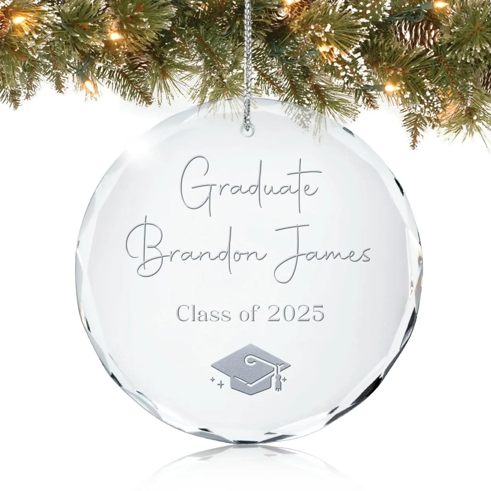 Personalized glass graduation ornament engraved with “Graduate,” a name, “Class of 2025,” and a graduation cap design, hanging on a Christmas tree.