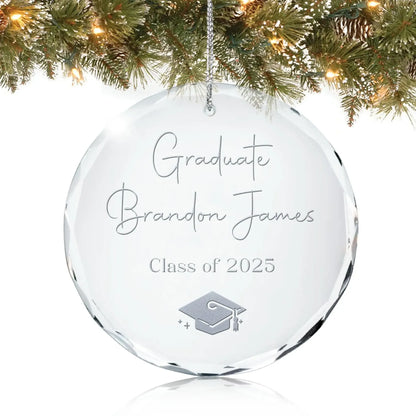 Personalized glass graduation ornament engraved with “Graduate,” a name, “Class of 2025,” and a graduation cap design, hanging on a Christmas tree.