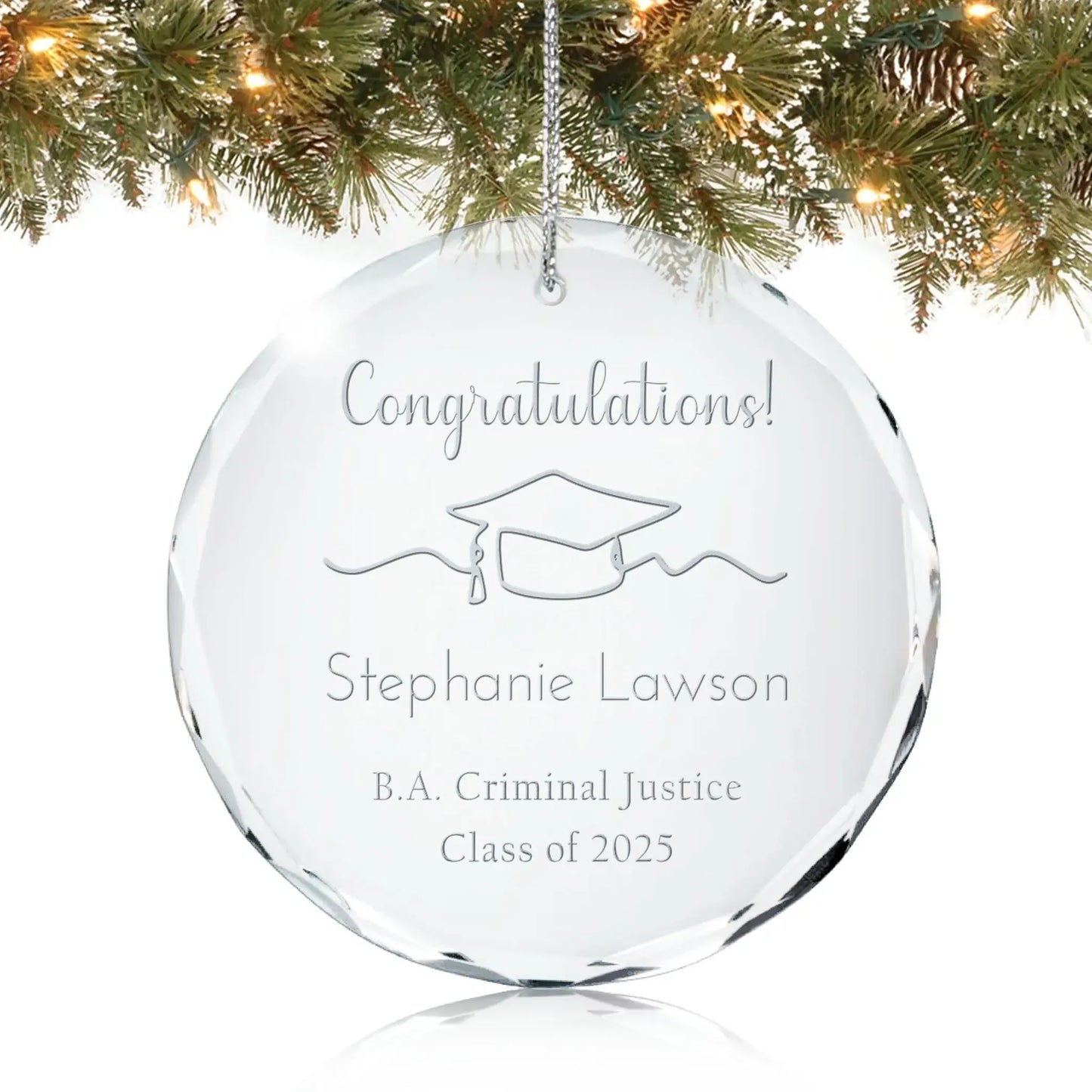 Personalized glass graduation ornament engraved with “Congratulations!” and a graduation cap design, hanging on a Christmas tree.