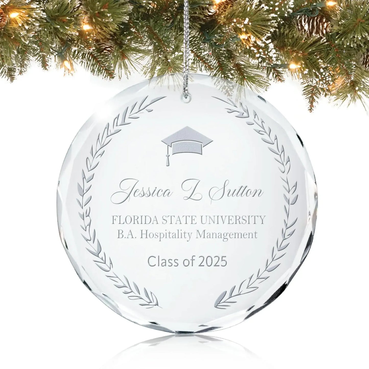 Personalized glass graduation ornament with laurel wreath design, engraved name, school, and “Class of 2025” hanging on a Christmas tree.