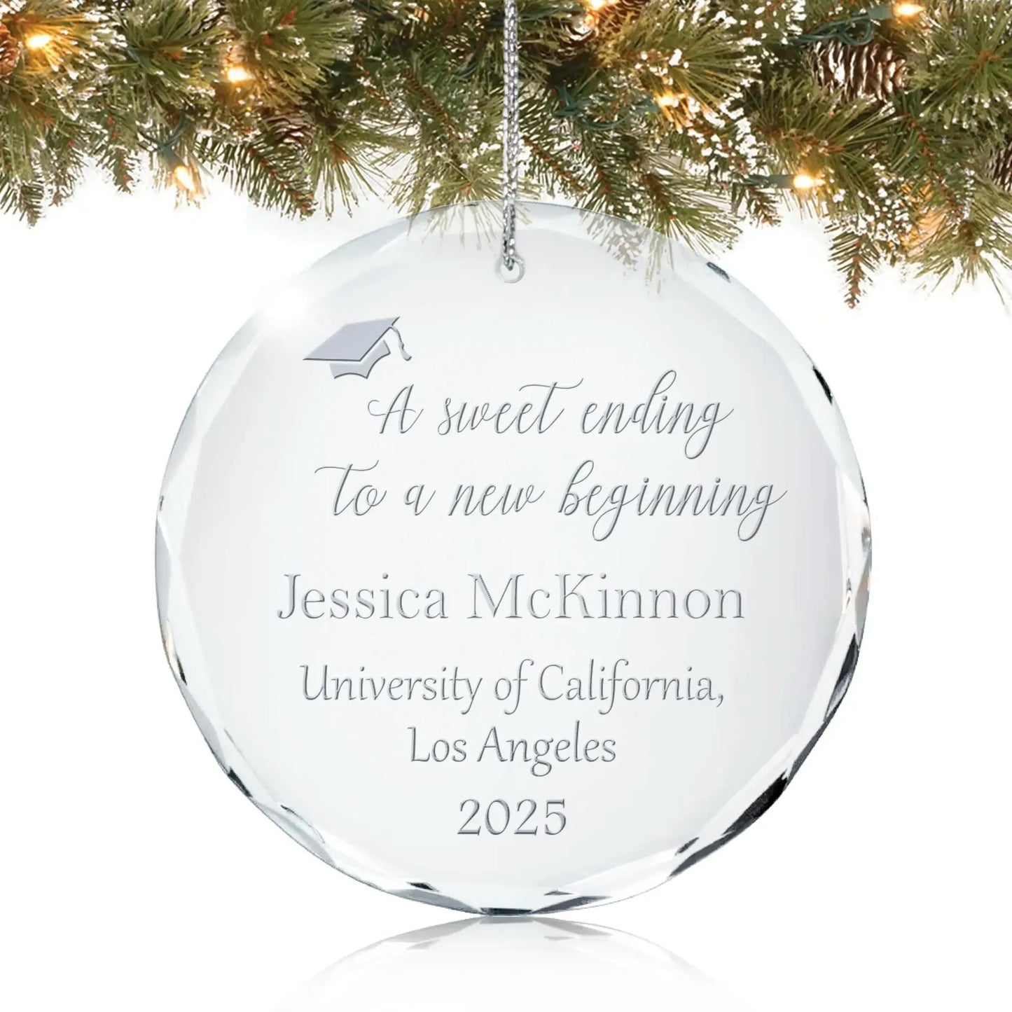 Personalized glass graduation ornament engraved with “A sweet ending to a new beginning” and graduation cap design hanging on a Christmas tree.