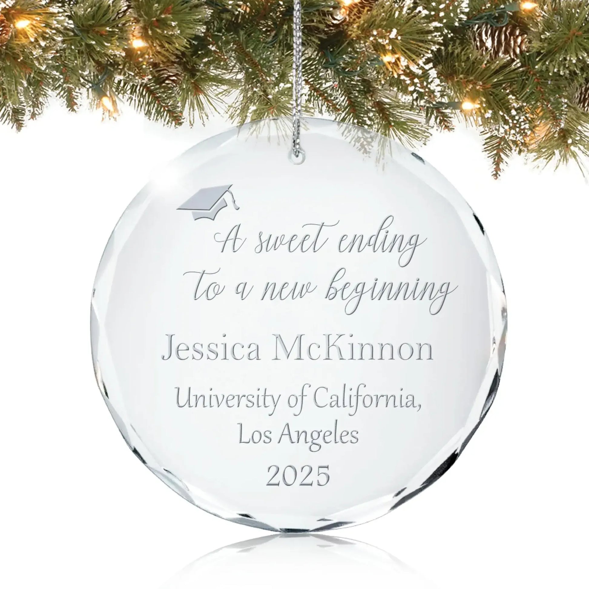Personalized glass graduation ornament engraved with “A sweet ending to a new beginning” and graduation cap design hanging on a Christmas tree.