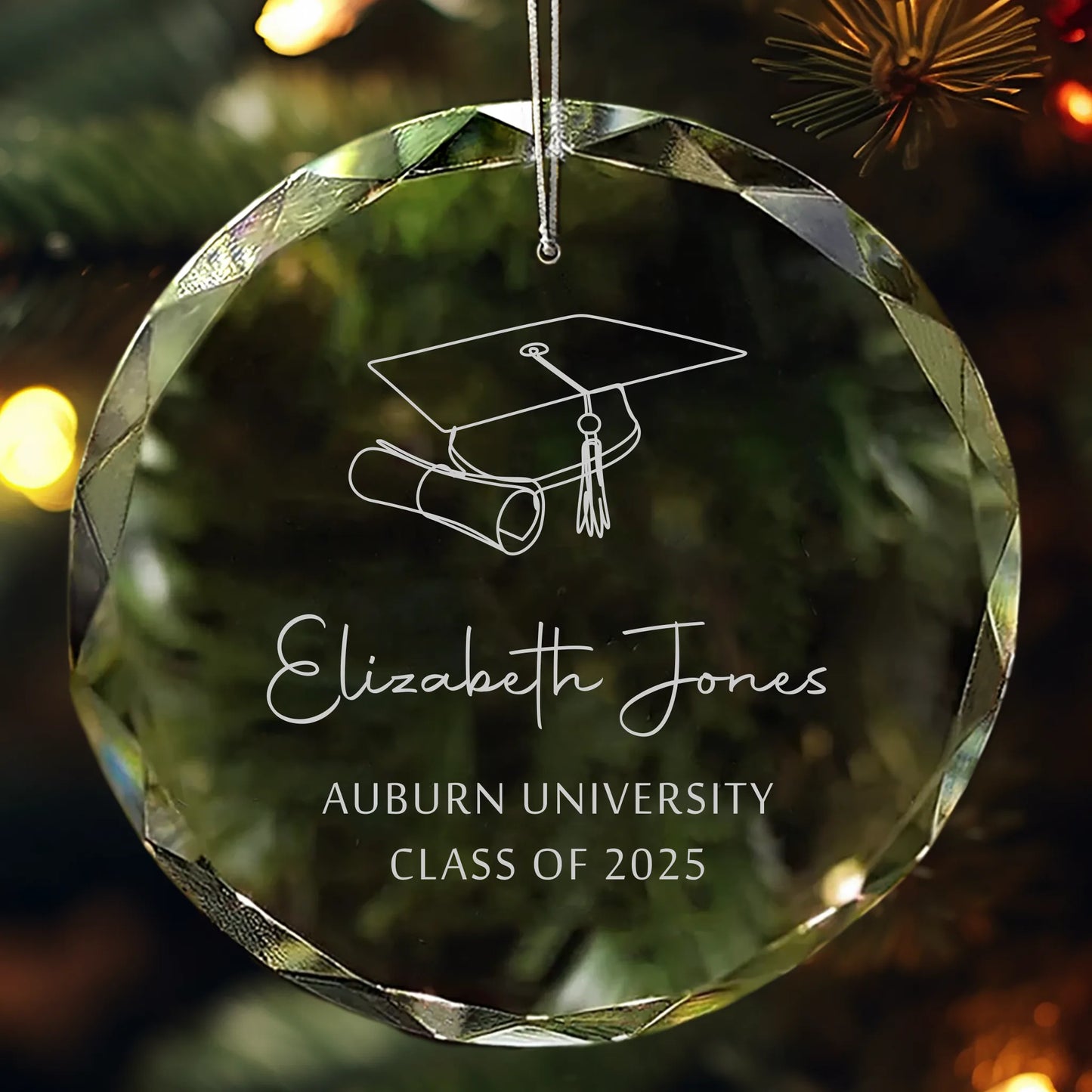 Personalized glass graduation ornament engraved with a cap, diploma, and “Class of 2025” hanging on a Christmas tree.
