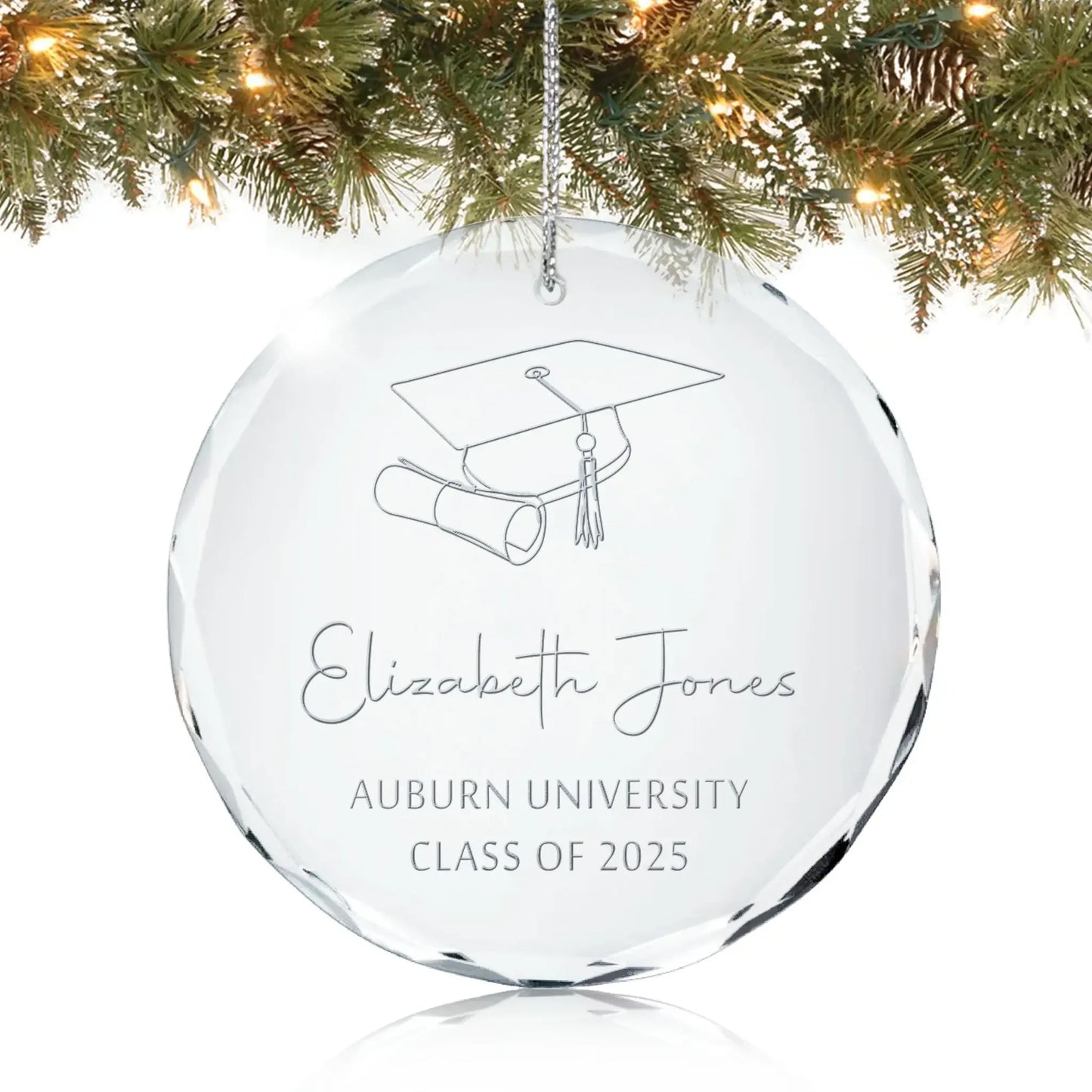Personalized glass graduation ornament engraved with a cap, diploma, and “Class of 2025” hanging on a Christmas tree.