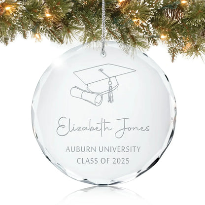 Personalized glass graduation ornament engraved with a cap, diploma, and “Class of 2025” hanging on a Christmas tree.