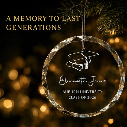 A personalized clear faceted glass graduation ornament hanging from a tree branch at night, with gold bokeh lights in the background. 