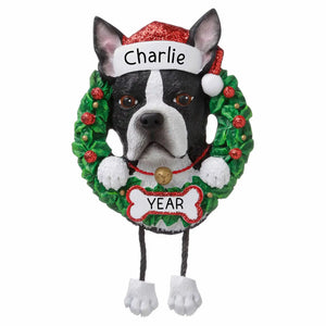 Personalized Boston Terrier Christmas ornament, the Boston Terrier head and paws in a green holly wreath wearing a red Santa hat with the pet name on the band, the year on a white bone below and two legs dangling beneath