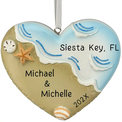 Heart-shaped ornament with beach design, sand, starfish, and shell, personalized with names and location.