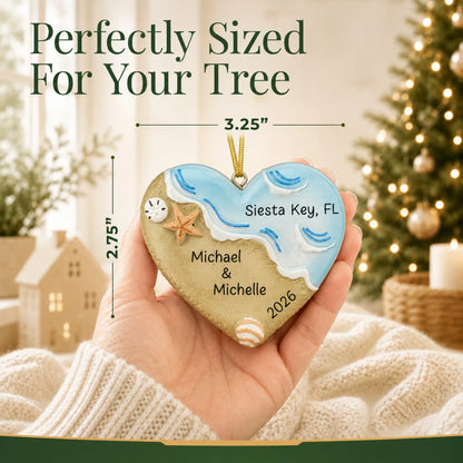 Size guide: the personalized name in sand beach christmas ornament is 3.25 in wide by 2.75 in tall, shown in hand