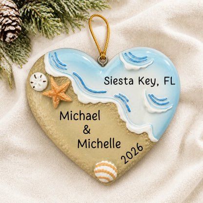 Personalized name in sand beach christmas ornament laid on a soft white knit blanket