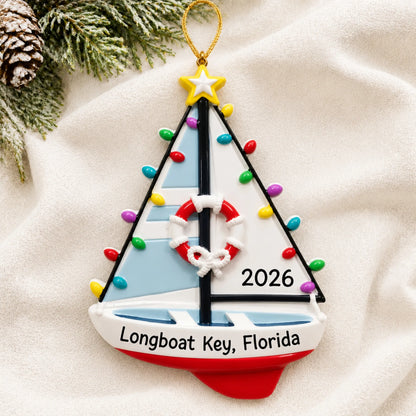 Personalized lighted sailboat christmas ornament laid on a soft white knit blanket