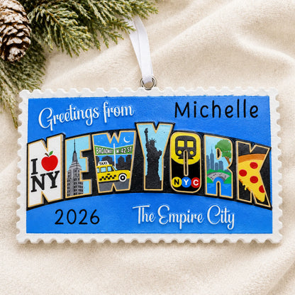 Personalized New York City postcard christmas ornament laid on a soft white knit blanket