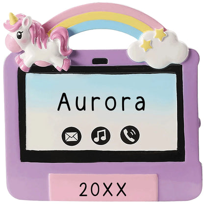 A personalized ornament in the shape of a purple and pink ipad with a unicorn, rainbow, and stars design. It includes a ribbon loop for hanging.