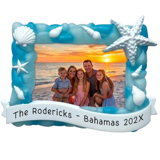 Personalized beach photo frame Christmas ornament with a sea glass blue shell-and-starfish frame holding a family beach photo, and a banner engraved with a custom name, destination, and year.
