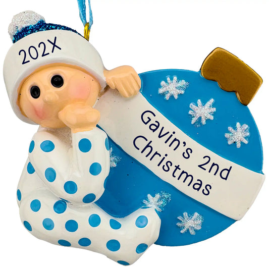Personalized baby boy Christmas ornament in blue, baby in polka dot pajamas hugging a blue ornament ball with a laser engraved two line banner