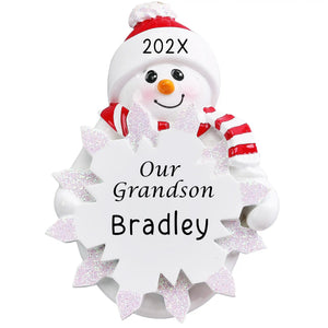 Our Grandson snowman personalized Christmas ornament with a smiling snowman in a red knit hat and striped scarf holding a glittered snowflake, the name engraved on the snowflake and the year on the hat