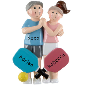 A personalized pickleball couple ornament with two figures holding pickleball paddles. The figures are adorned with customizable names and year