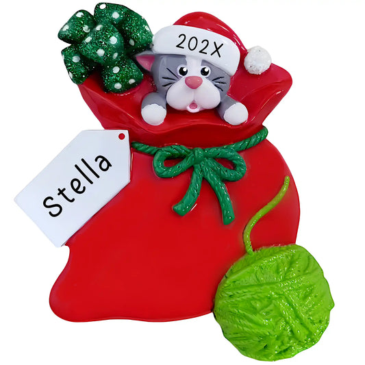 Personalized cat ornament with gray kitten in Santa hat peeking out of red gift bag, name engraved on gift tag and year on yarn ball
