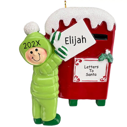 A personalized Christmas ornament of a child in a green snowsuit mailing a letter to Santa in a red mailbox, with space for a custom name.