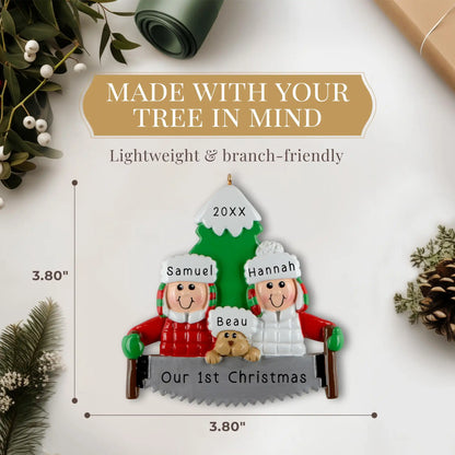 A personalized resin ornament featuring a couple in winter clothing with a dog, standing in front of a Christmas tree. The ornament includes customizable text for names and a year. The image shows the size 3.80 by 3.80 inches.