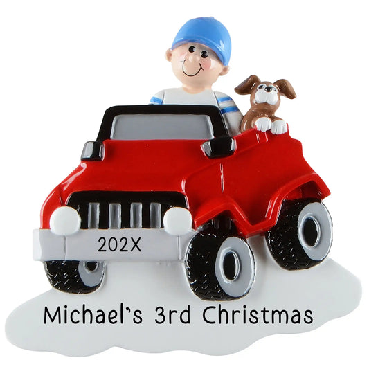A personalized Christmas ornament of a boy and a dog in a red ride on electric jeep, featuring a white base for a custom engraved name and year.