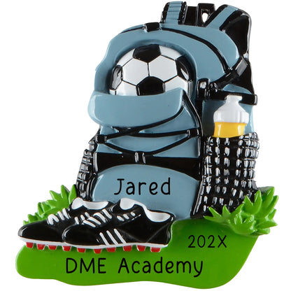 A personalized Christmas ornament of a blue soccer equipment bag with a ball and water bottle next to black cleats, with a custom name and team name.