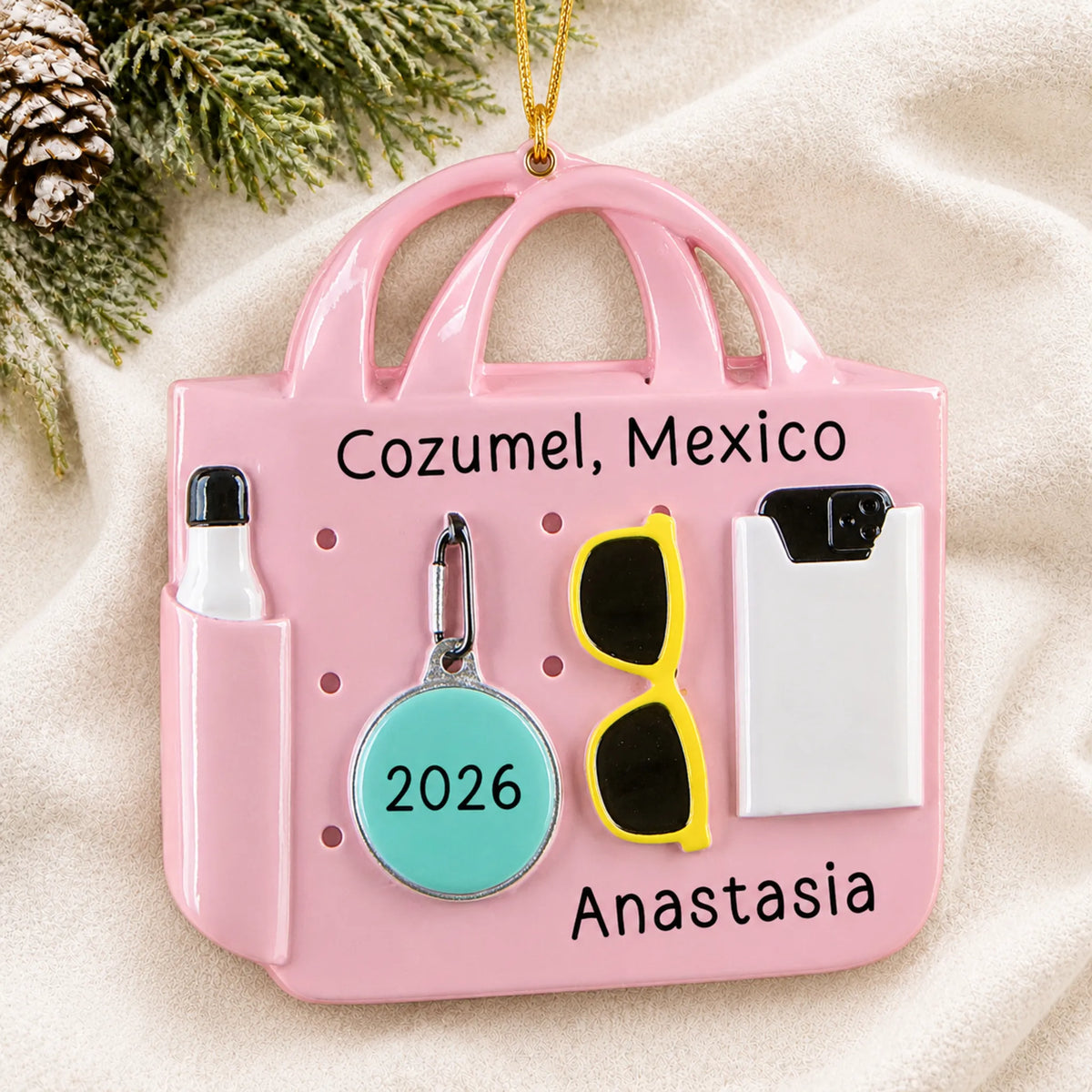 Personalized pink beach bag christmas ornament laid on a soft white knit blanket