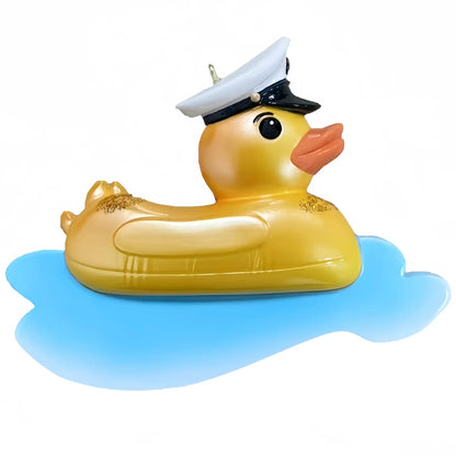 A personalized Christmas ornament of a yellow rubber duck float wearing a captain's hat on blue water, with space on the side for a custom-engraved name.