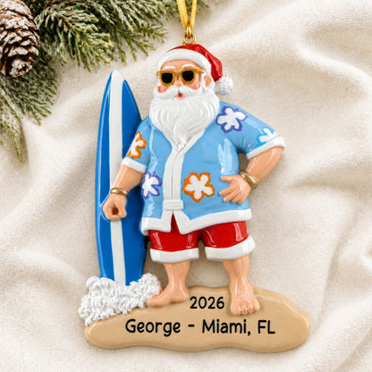 Personalized surfing Santa christmas ornament laid on a soft white knit blanket