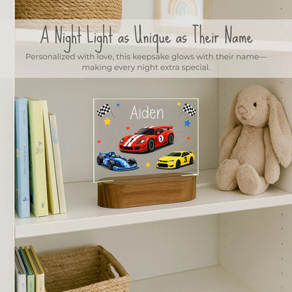 Custom name race car night light on boys bookshelf, acrylic plate with red blue and yellow race cars and checkered flags, name Aiden laser engraved, warm LED glow on acacia wood base