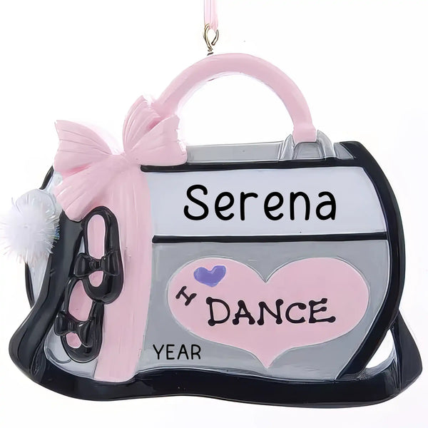 Personalized Christmas ornament shaped like a grey dance bag with a pink bow, black ballet slippers, and a pink heart reading "I Love Dance," with a blank surface ready for custom name engraving.