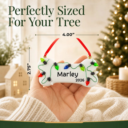 Size guide: the personalized Christmas Lights Dog Bone ornament is 4.00 in wide by 2.75 in tall, shown in hand