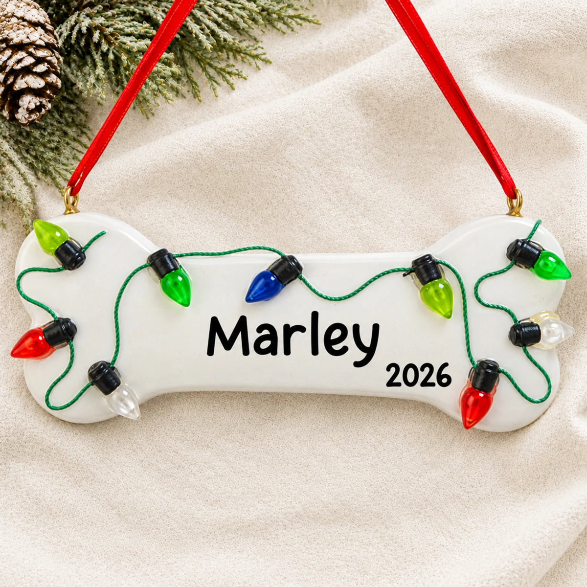 Personalized Christmas Lights Dog Bone ornament laid on a soft white knit blanket