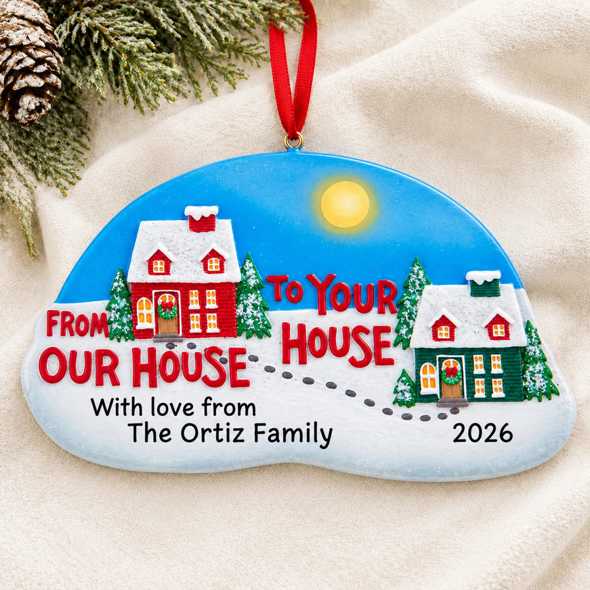 Personalized From Our House to Yours christmas ornament laid on a soft white knit blanket