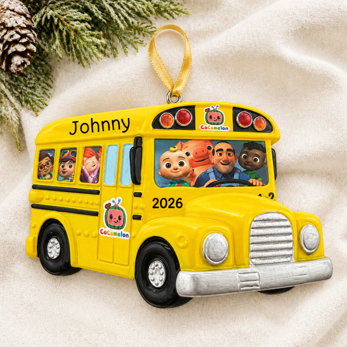 Personalized CoComelon School Bus christmas ornament laid on a soft white knit blanket