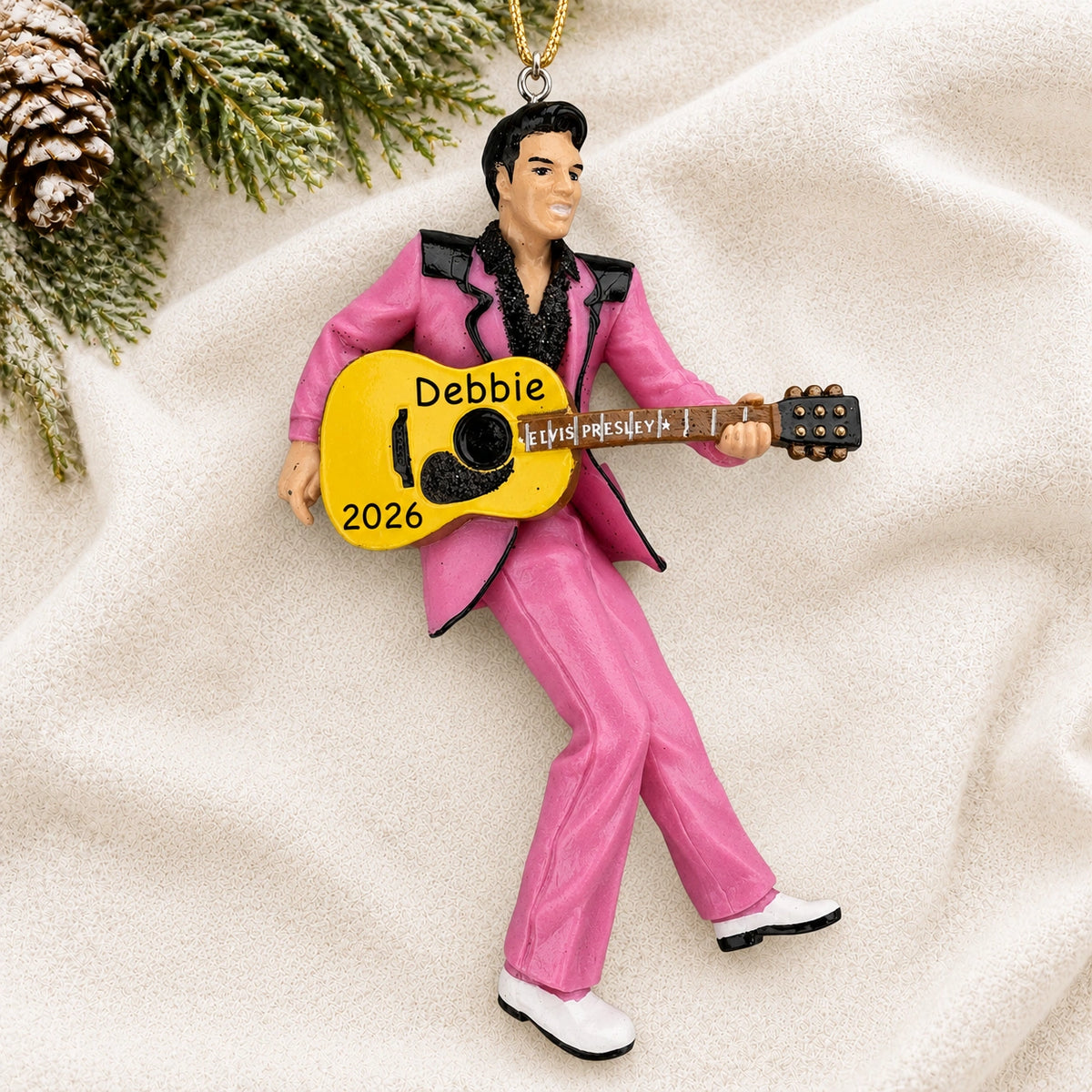 Personalized Elvis Presley guitar Christmas ornament reading Debbie 2026 on a white knit blanket with pine