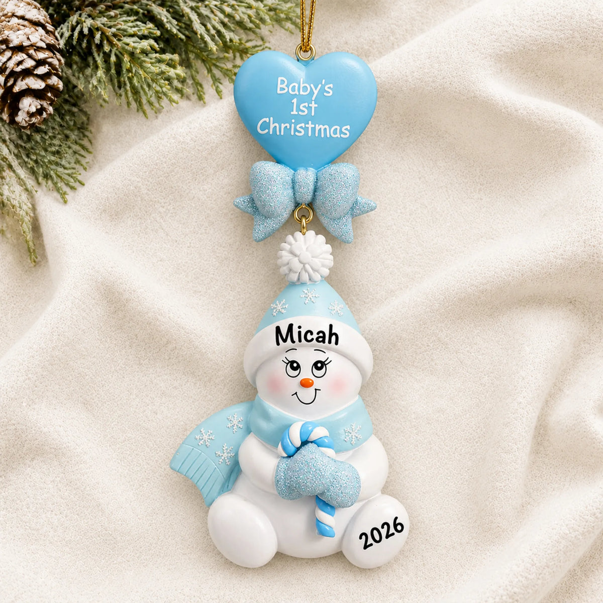 Personalized blue baby's 1st christmas candy cane snowbaby ornament laid on a soft white knit blanket