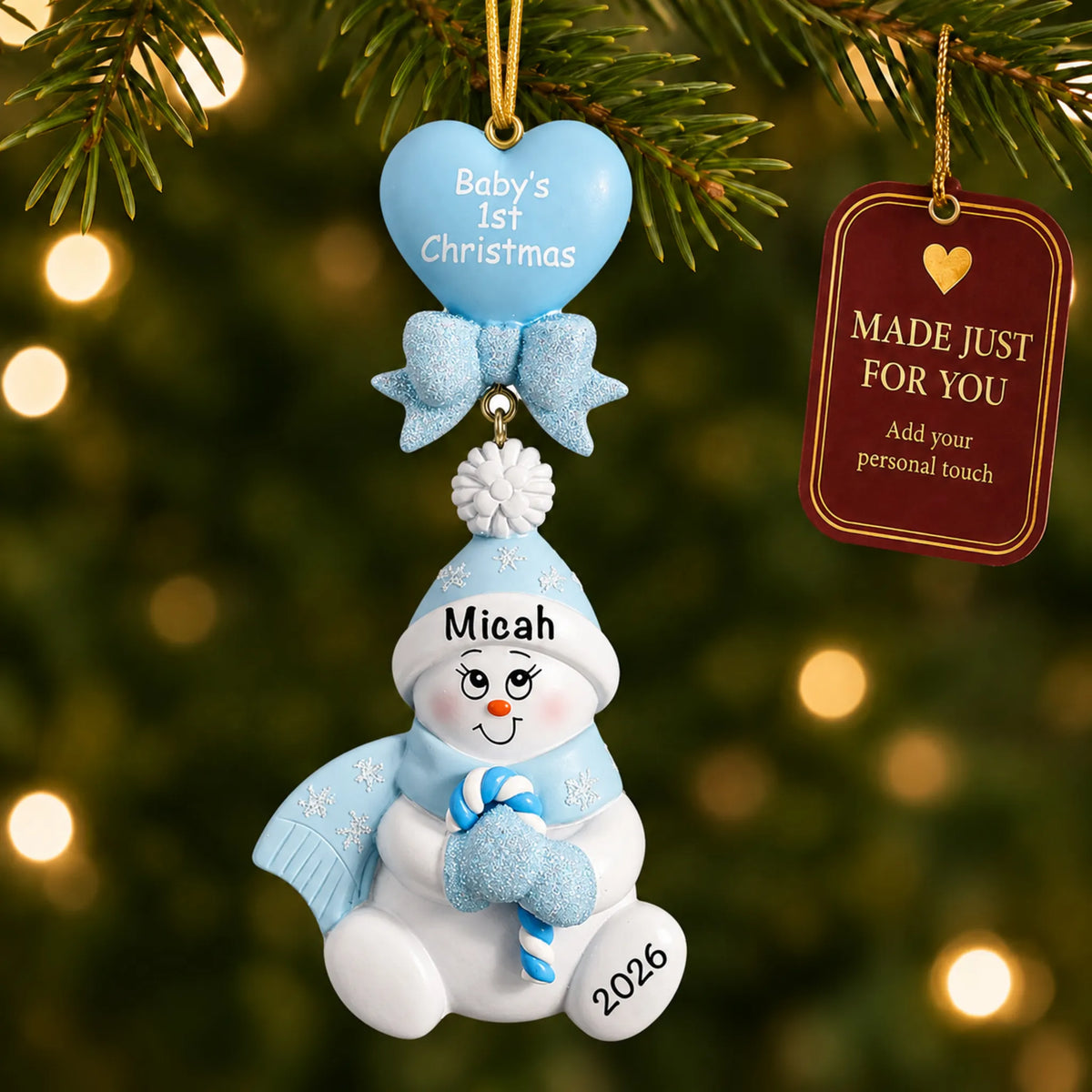 Blue baby's 1st christmas candy cane snowbaby ornament hanging on a lit Christmas tree with a Made Just For You gift tag