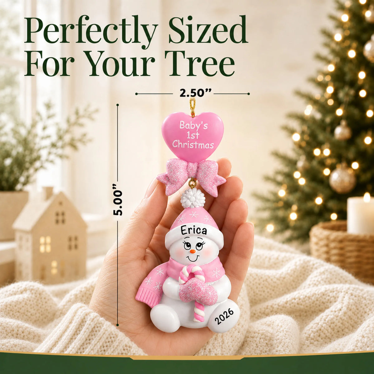Size guide: the personalized pink baby's 1st christmas candy cane snowbaby ornament shown in hand next to a Christmas tree