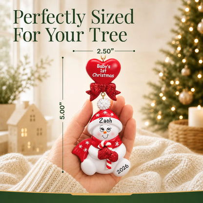 Size guide: the personalized red baby's 1st christmas candy cane snowbaby ornament shown in hand next to a Christmas tree