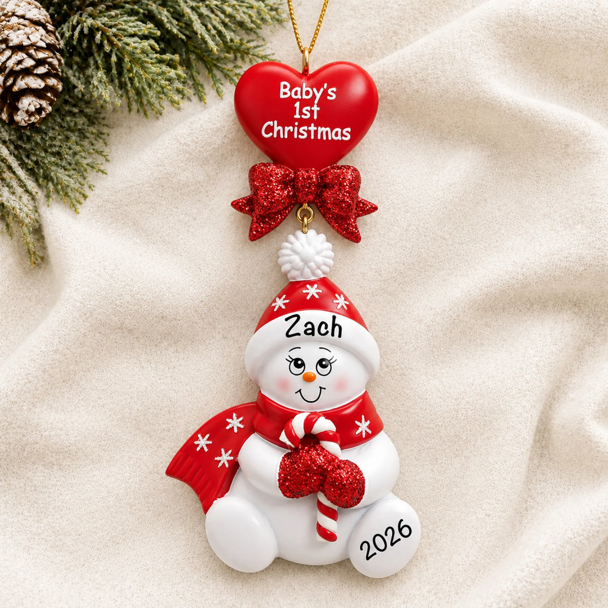 Personalized red baby's 1st christmas candy cane snowbaby ornament laid on a soft white knit blanket