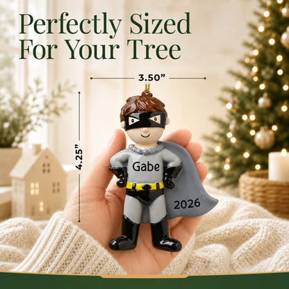 Size guide: the personalized caped super hero christmas ornament is 3.50 in wide by 4.25 in tall, shown in hand