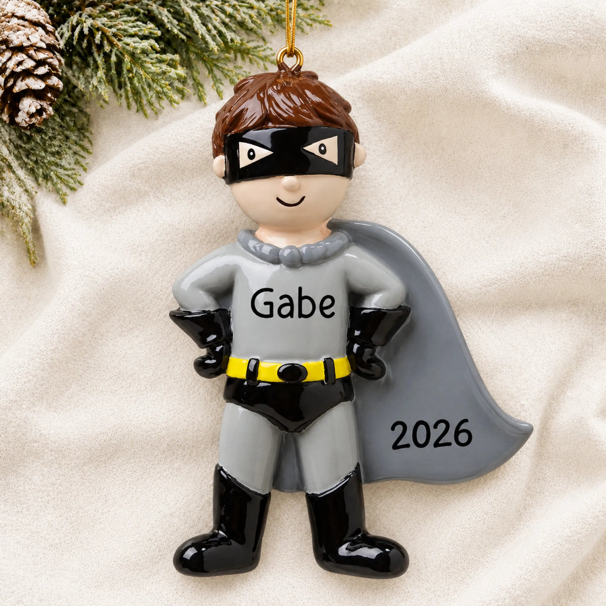 Personalized caped super hero christmas ornament laid on a soft white knit blanket