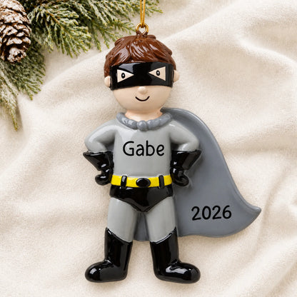 Personalized caped super hero christmas ornament laid on a soft white knit blanket