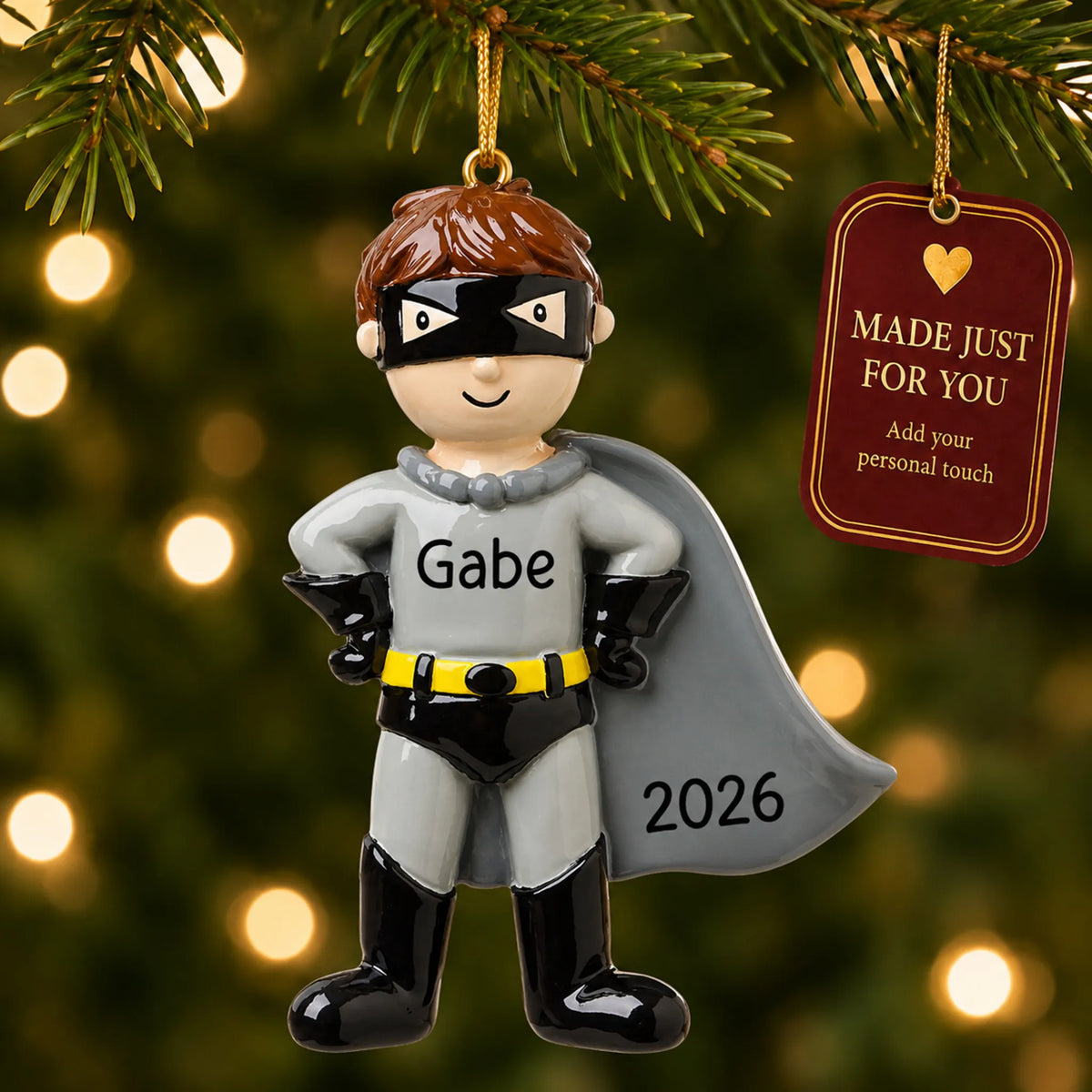 Caped super hero christmas ornament hanging on a lit Christmas tree with a Made Just For You gift tag