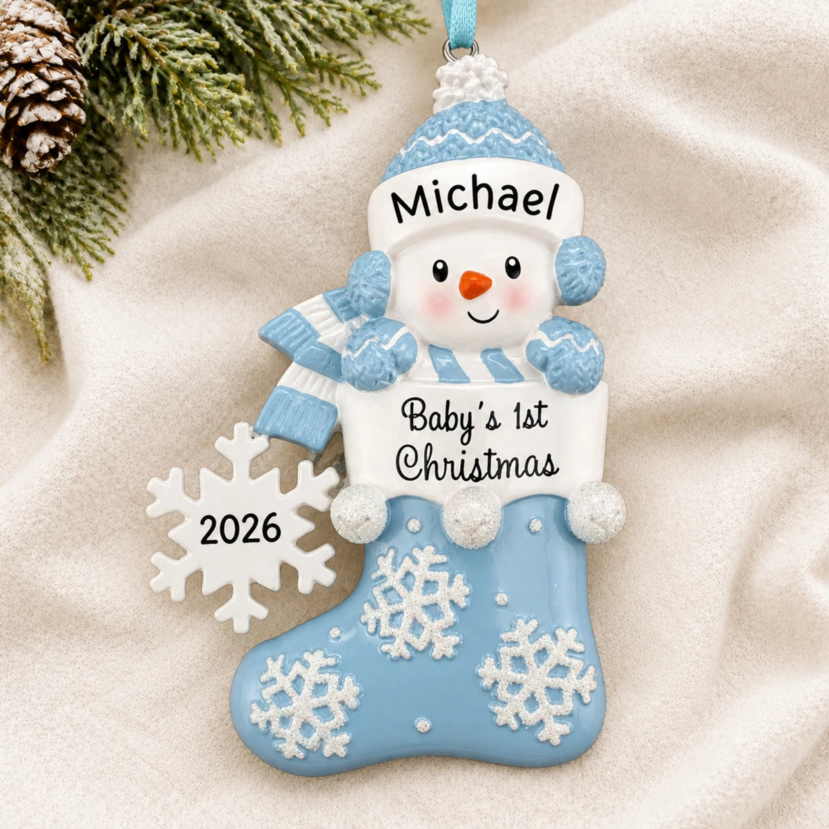 Personalized blue snowman baby's 1st christmas ornament laid on a soft white knit blanket