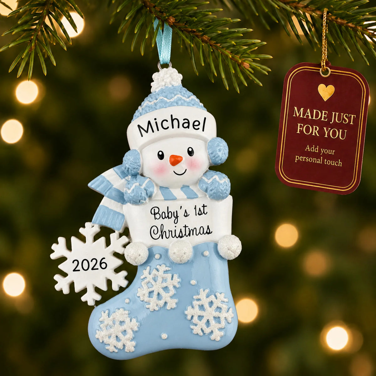 Blue snowman baby's 1st christmas ornament hanging on a lit Christmas tree with a Made Just For You gift tag