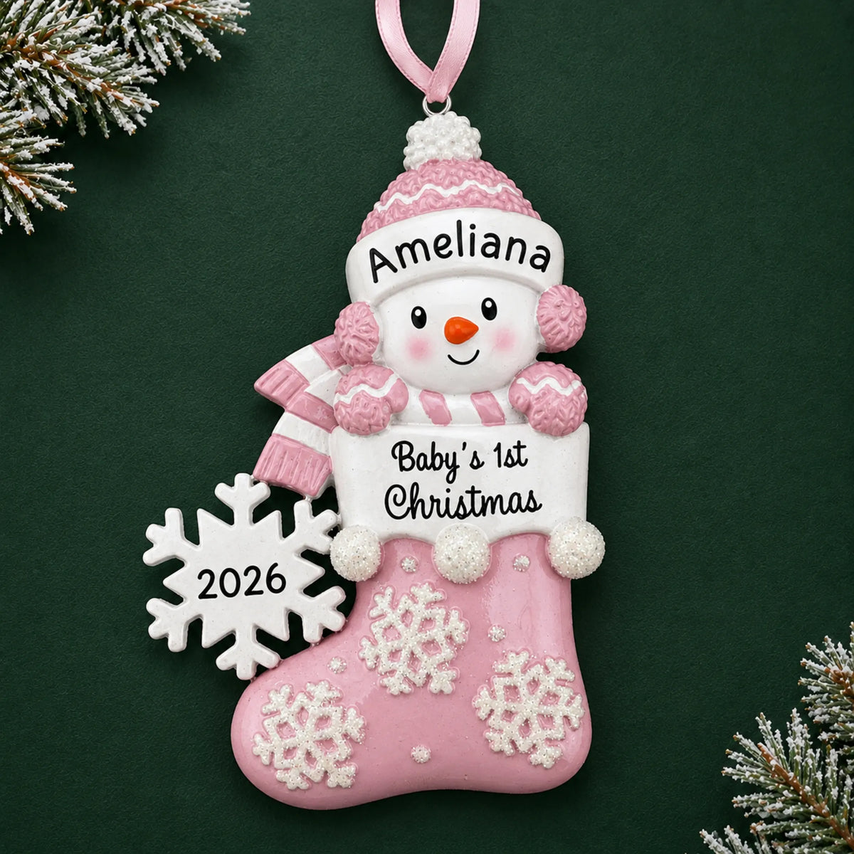 Personalized pink snowman baby's 1st christmas ornament on a dark green pine background